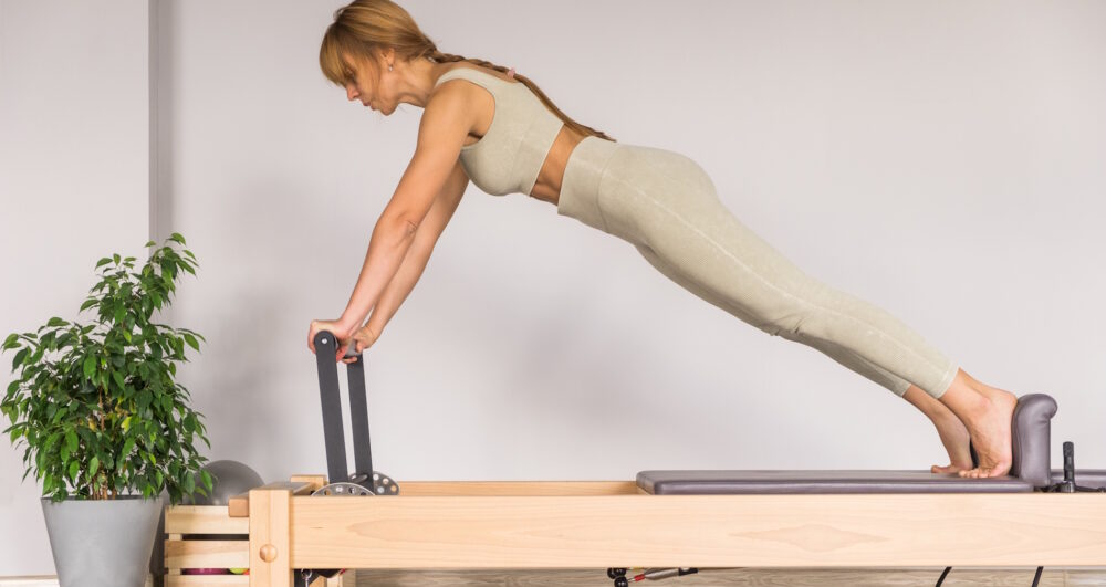 Woman training pilates on the reformer bed. Reformer pilates studio machine for fitness workouts in gym. Fit, healthy and strong authentical body. Fitness concept.